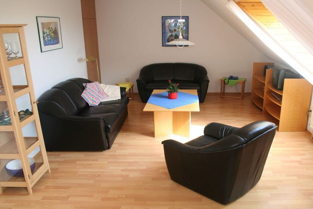 A loft-style living space with a black leather sofa, a wooden coffee table with a red pot, and a bookshelf.