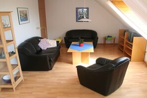 Un espacio habitable estilo loft con un sofá de cuero negro, una mesa de centro de madera con una maceta roja y una estantería.