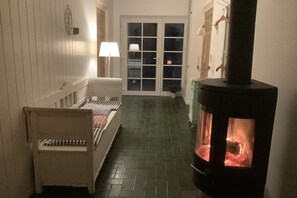 Passadís estret amb un llit, una cadira, una llar de foc i una porta que dona a zona exterior.