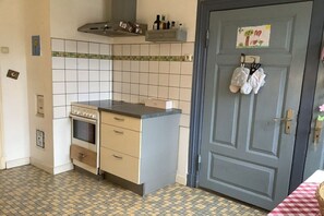 A compact kitchen with a tiled backsplash, a built-in oven, and a blue door with a small artwork. - House on the Westerdeich (Vollerwiek)