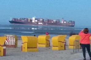 Ein Strand mit gelben Liegestühlen und einem großen Frachtschiff im Hintergrund.