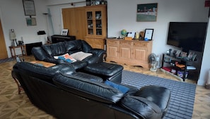 A living room with a black leather sofa, a wooden cabinet, a television, and a globe on a shelf. - Bungalow Annex - Sleeps 6 With Countryside Views (Tarporley)