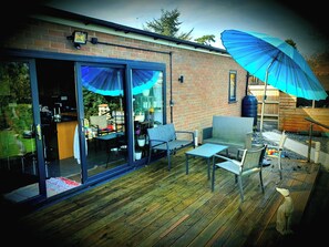 A patio area with a glass door leading to a kitchen, a blue umbrella, and outdoor furniture. - Bungalow Annex - Sleeps 6 With Countryside Views (Tarporley)