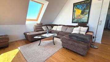 A modern living room with a sectional sofa, a glass coffee table, and a poster of Vincent van Gogh's 'Café de Nuit' on the wall.