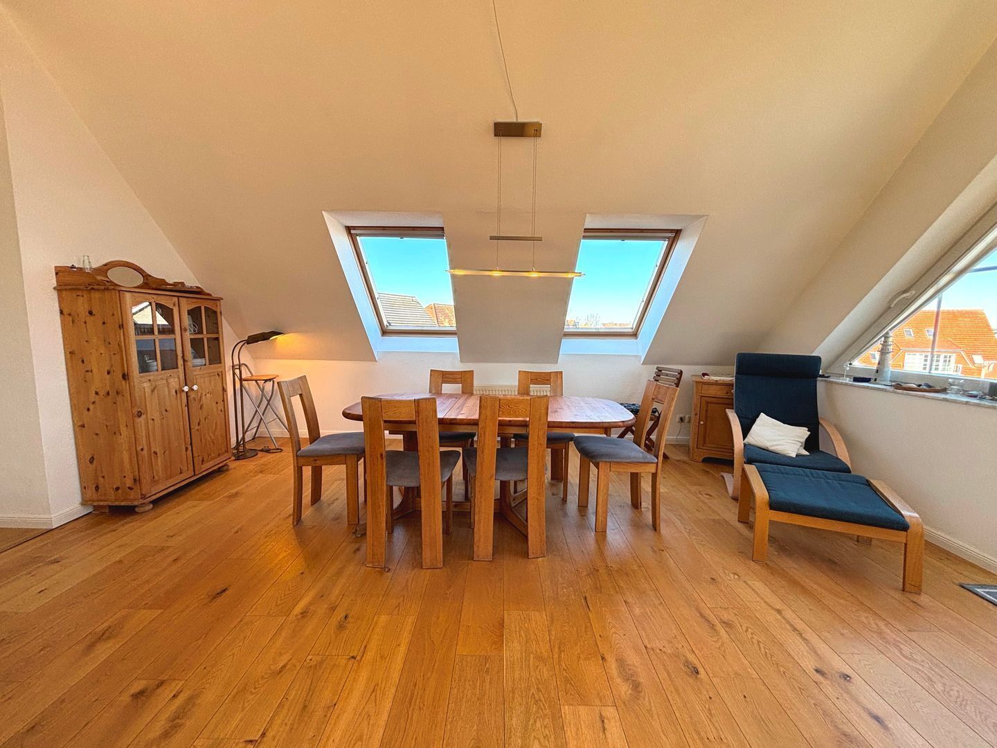 Una habitación con una mesa de comedor de madera, sillas, un sofá y un armario. Hay tragaluces en el techo.