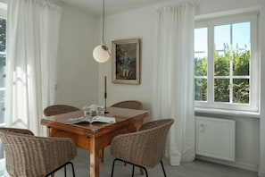 A dining area with a wooden table, four wicker chairs, a hanging light fixture, and a framed painting on the wall. - Cozy Vacation Rental at Friesenring 17c in Wenningstedt (Wenningstedt-Braderup (Sylt))