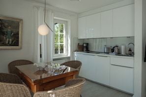 A modern kitchen with white cabinets, a dining table with wicker chairs, and a painting on the wall. - Cozy Vacation Rental at Friesenring 17c in Wenningstedt (Wenningstedt-Braderup (Sylt))