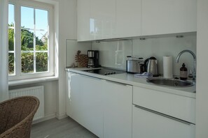 A modern kitchen with white cabinets, a stainless steel sink, a kettle, a coffee maker, and a wicker chair. - Cozy Vacation Rental at Friesenring 17c in Wenningstedt (Wenningstedt-Braderup (Sylt))