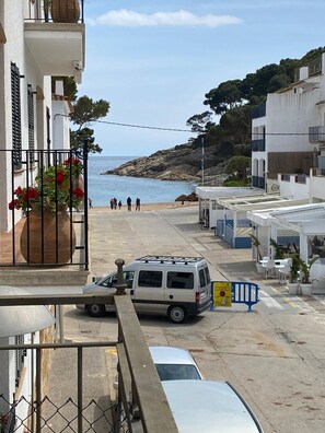 A coastal street with a white van parked on the side, a clear view of the sea, and a few people walking.