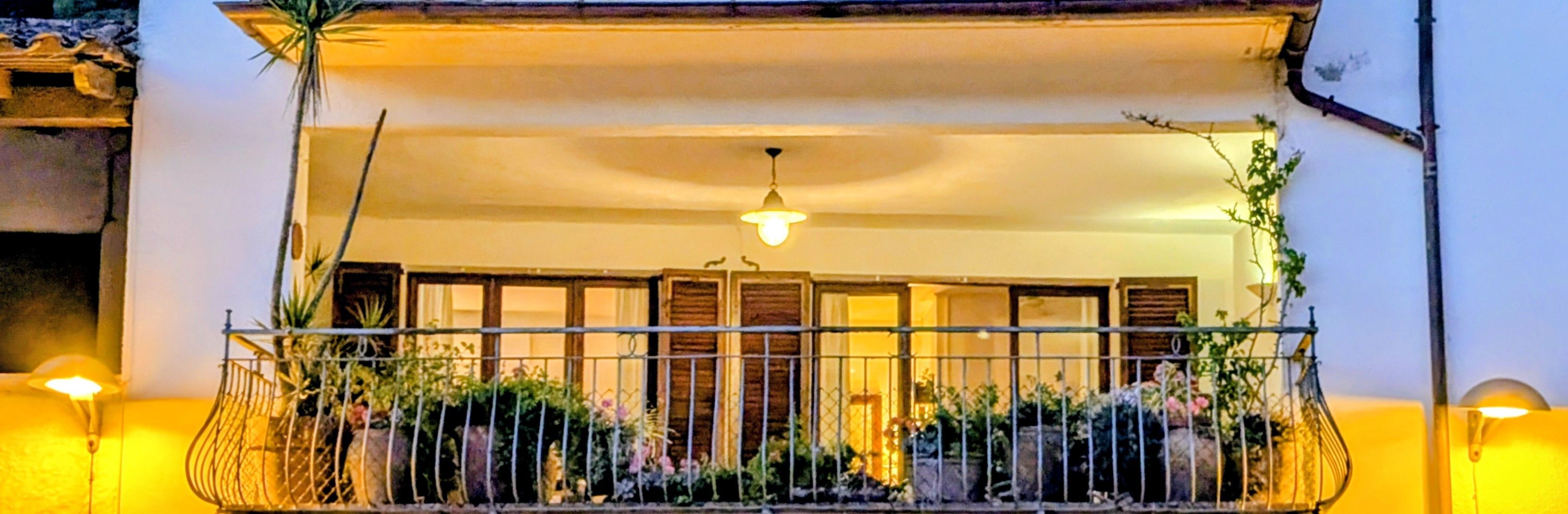 Un balcon doté d’une rambarde en métal, de plantes en pot et d’un luminaire suspendu.