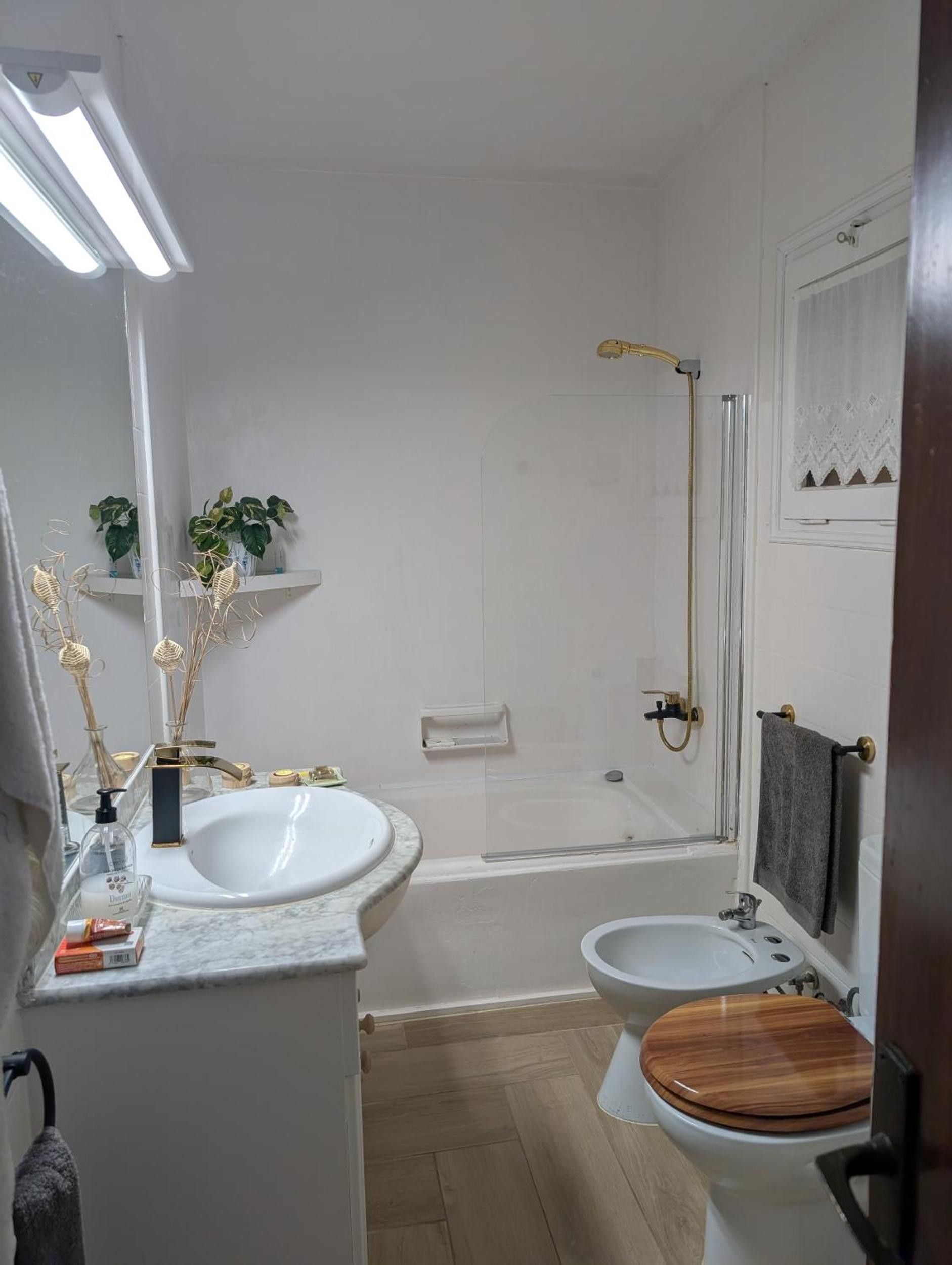 Une salle de bain avec une baignoire, des toilettes et un lavabo. On y trouve des plantes sur une étagère et un porte-serviettes.