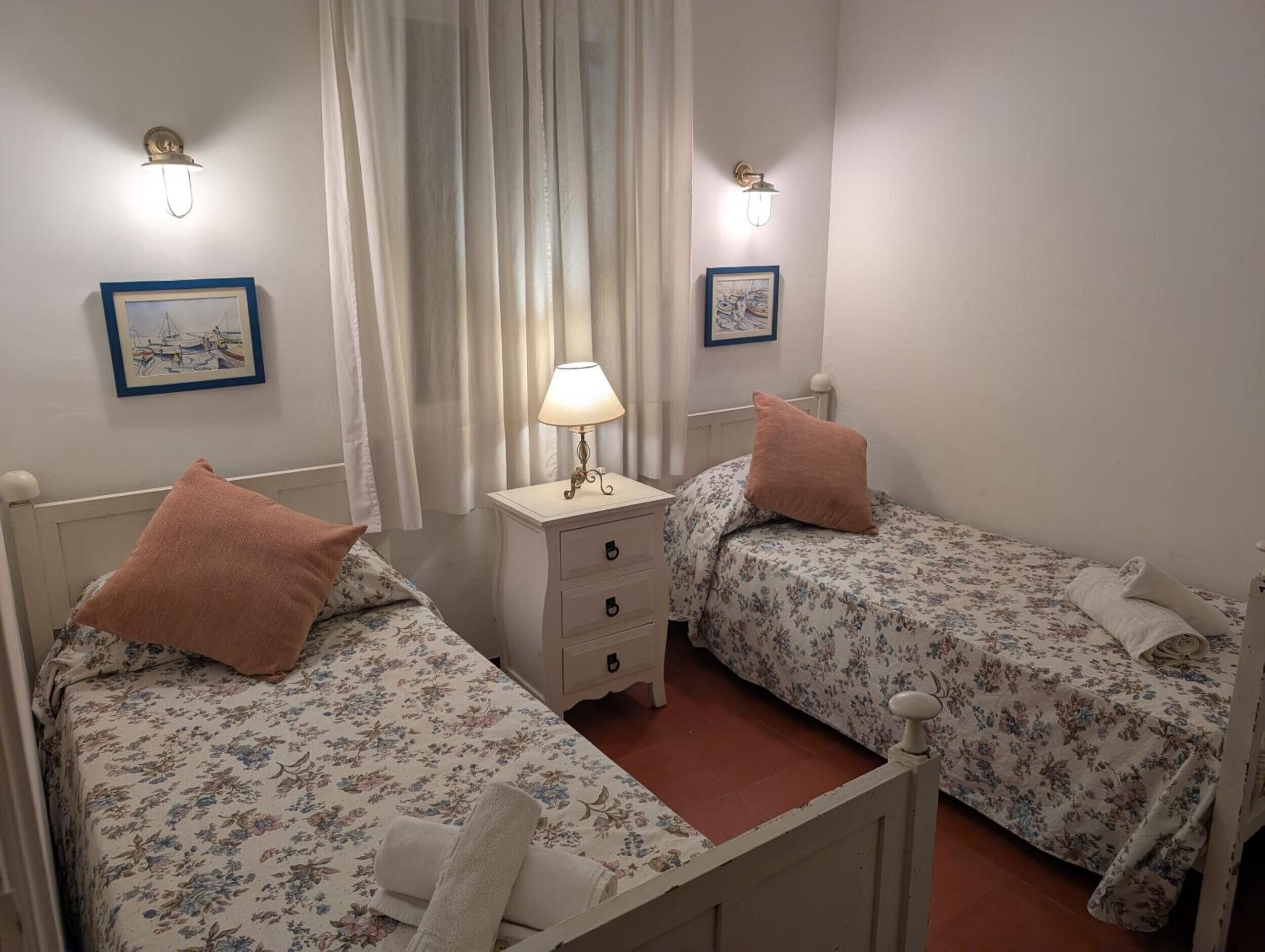 Une chambre avec deux lits simples, une table de chevet avec une lampe et deux appliques murales.