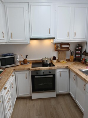 Een keuken met witte kastjes, een magnetron, een fornuis en een spoelbak.