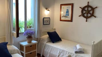 Un dormitorio con dos camas individuales, una ventana con cortinas, una rueda de barco montada en la pared y un cuadro enmarcado.