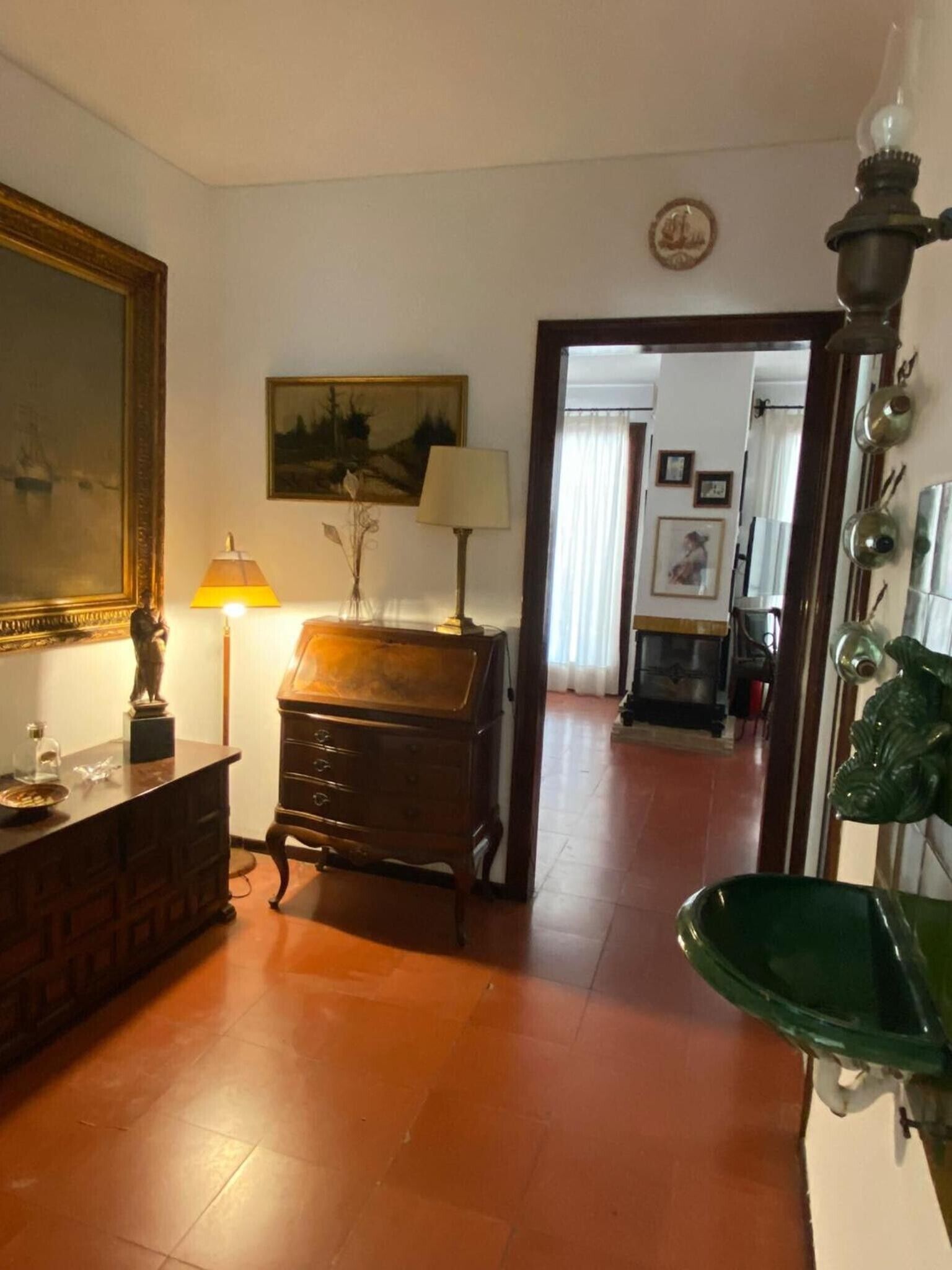Una habitación con un aparador de madera, una lámpara, un cuadro y un florero verde.