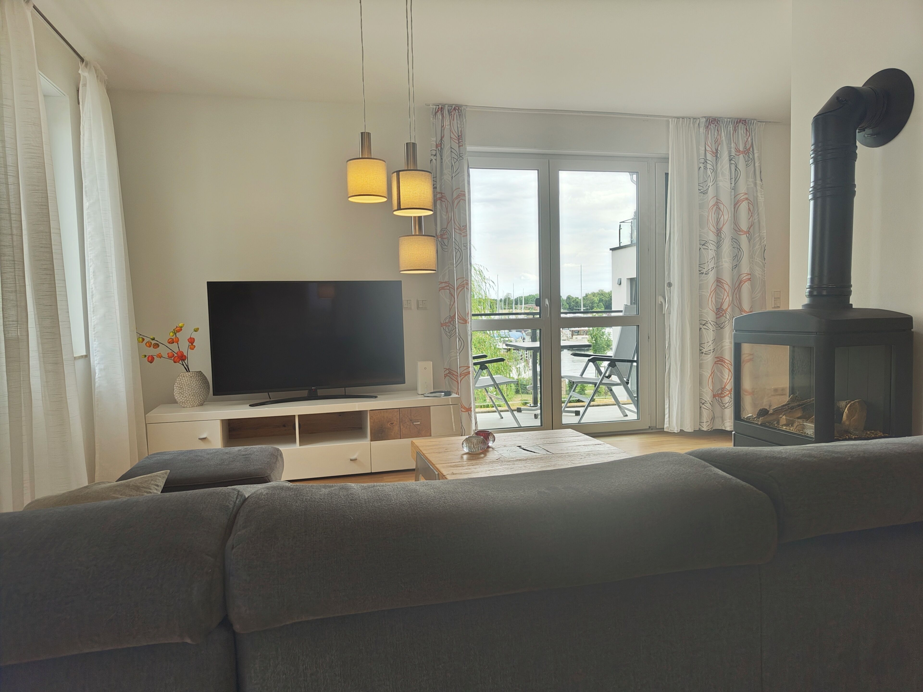 A living room with a sofa, a flat-screen TV, a fireplace, and a balcony with outdoor furniture.