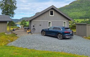 A modern two-story building with a gravel driveway, a parked car, and a scenic view of a lake and mountains. - Stunning home in Stongfjorden with house a panoramic view (Stongfjorden)