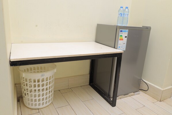 A small kitchenette area with a white countertop, a black-framed refrigerator, and a white laundry basket.
