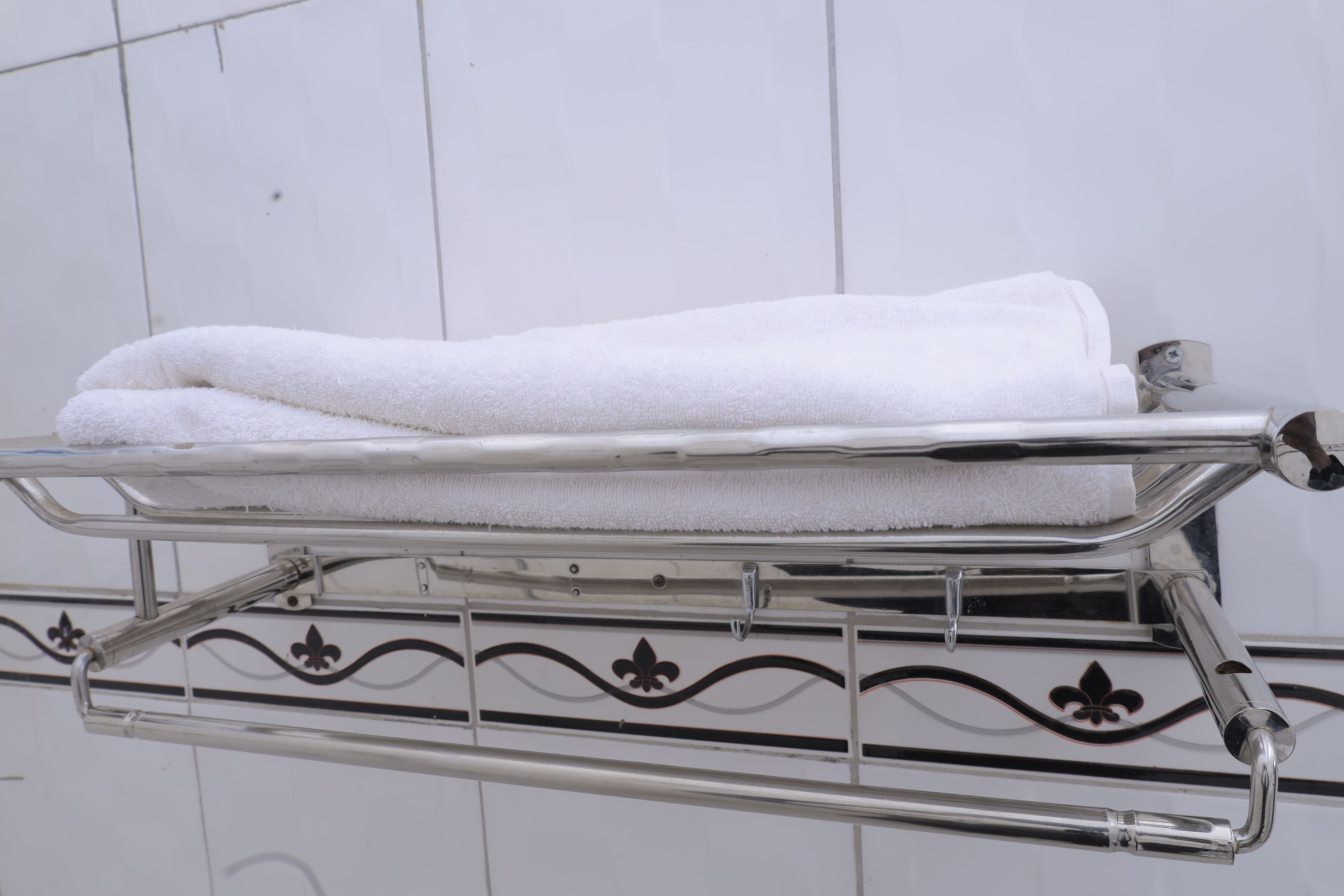 A white towel folded on a chrome towel rack with a decorative pattern.