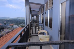 A balcony with a view of a hilly landscape, a chair, and a door leading to an interior space.
