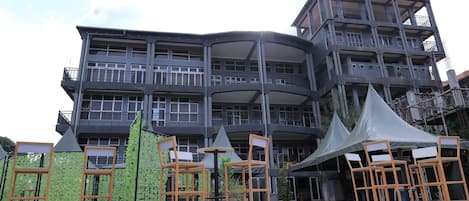 A multi-story building with balconies, outdoor seating, and a covered area with chairs.