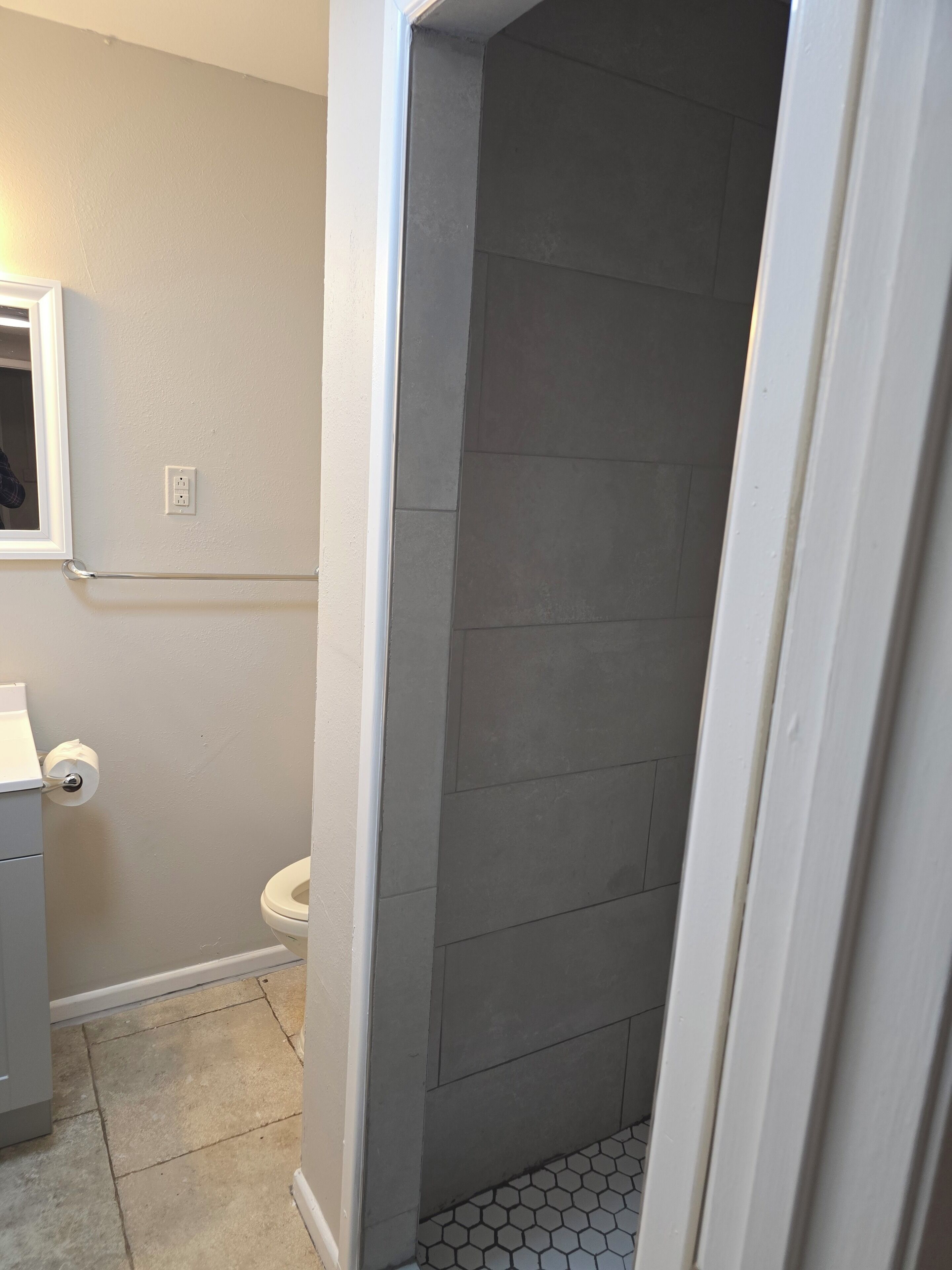 A bathroom with a toilet, a towel rack, and a shower area with tiled walls.