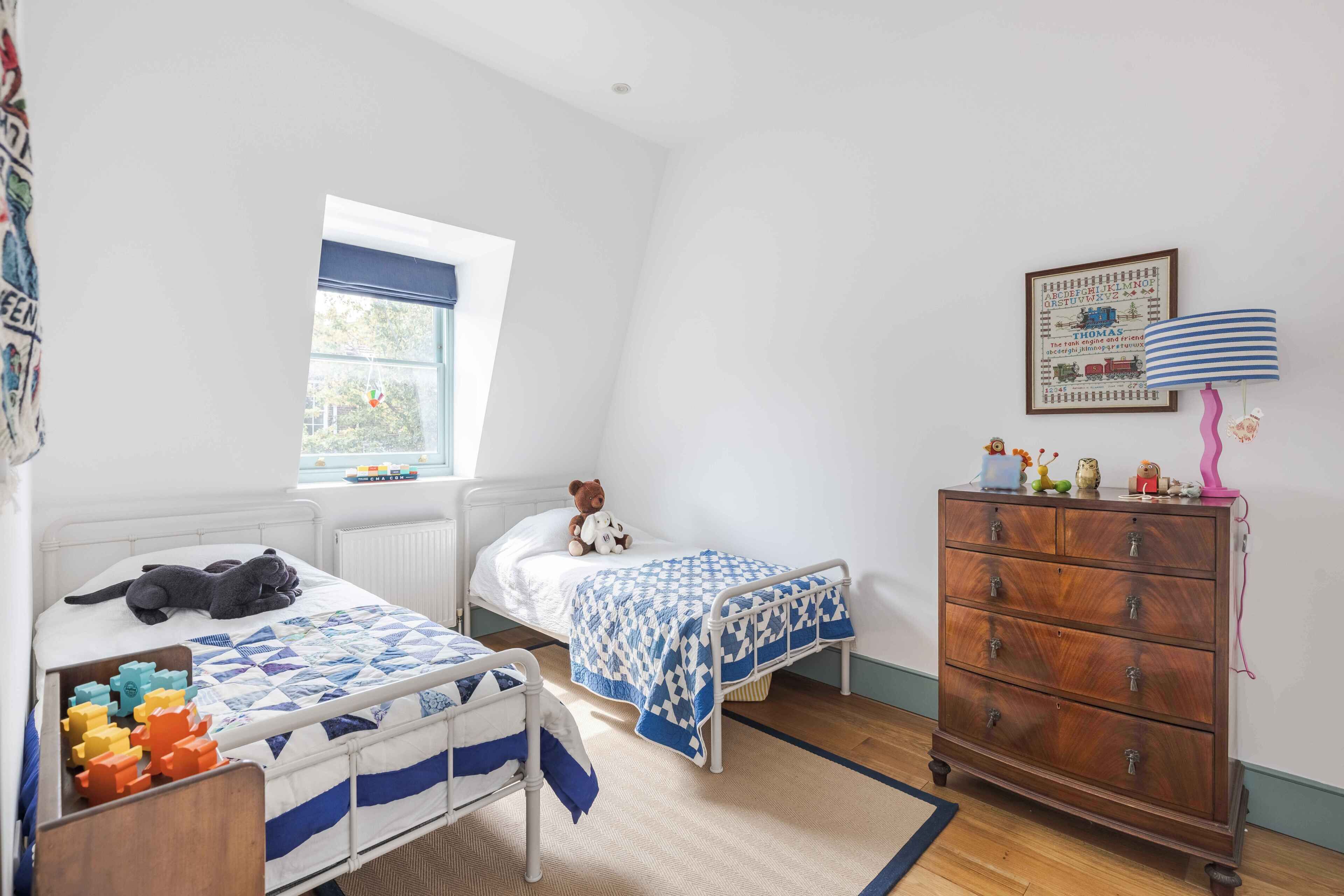Habitación infantil con dos camas, un aparador, una ventana y un adorno en la pared.