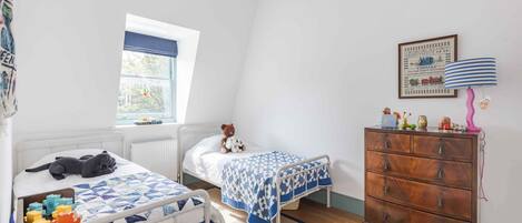 Habitación infantil con dos camas, un aparador, una ventana y un adorno en la pared.