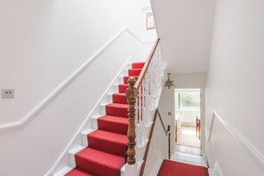 Eine Treppe mit roten Teppichstufen und weißen Geländern, die zu einem Raum mit Heizkörper und Tür führt.