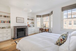 Ein Schlafzimmer mit einem großen Bett, einem Kamin, einem Schreibtisch und Bücherregalen.