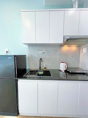 A kitchen with a black refrigerator, a sink with a green colander, and a coffee maker on the counter. - Midmost C22 Hotel & Apartment (Ninh Kieu)