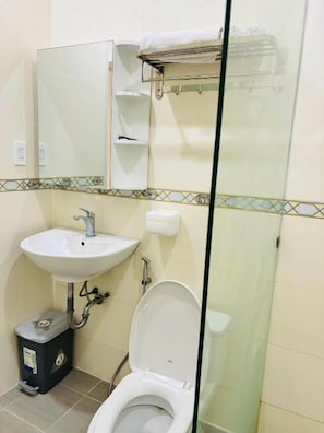 Une salle de bain avec un lavabo blanc, des toilettes, un miroir et une douche à parois de verre.