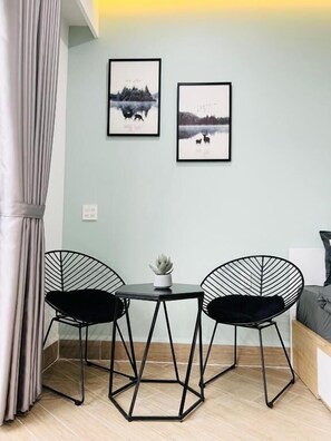 Une pièce comprenant un lit, deux chaises, une petite table avec une plante et deux tableaux encadrés accrochés au mur.