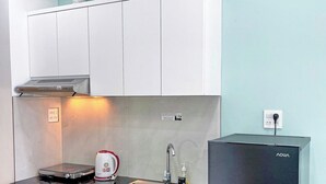 Une cuisine de taille réduite avec des meubles blancs, un réfrigérateur noir et un évier en acier inoxydable.