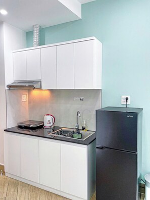 Una cucina compatta con mobili bianchi, un frigorifero nero e un lavello in acciaio inossidabile.