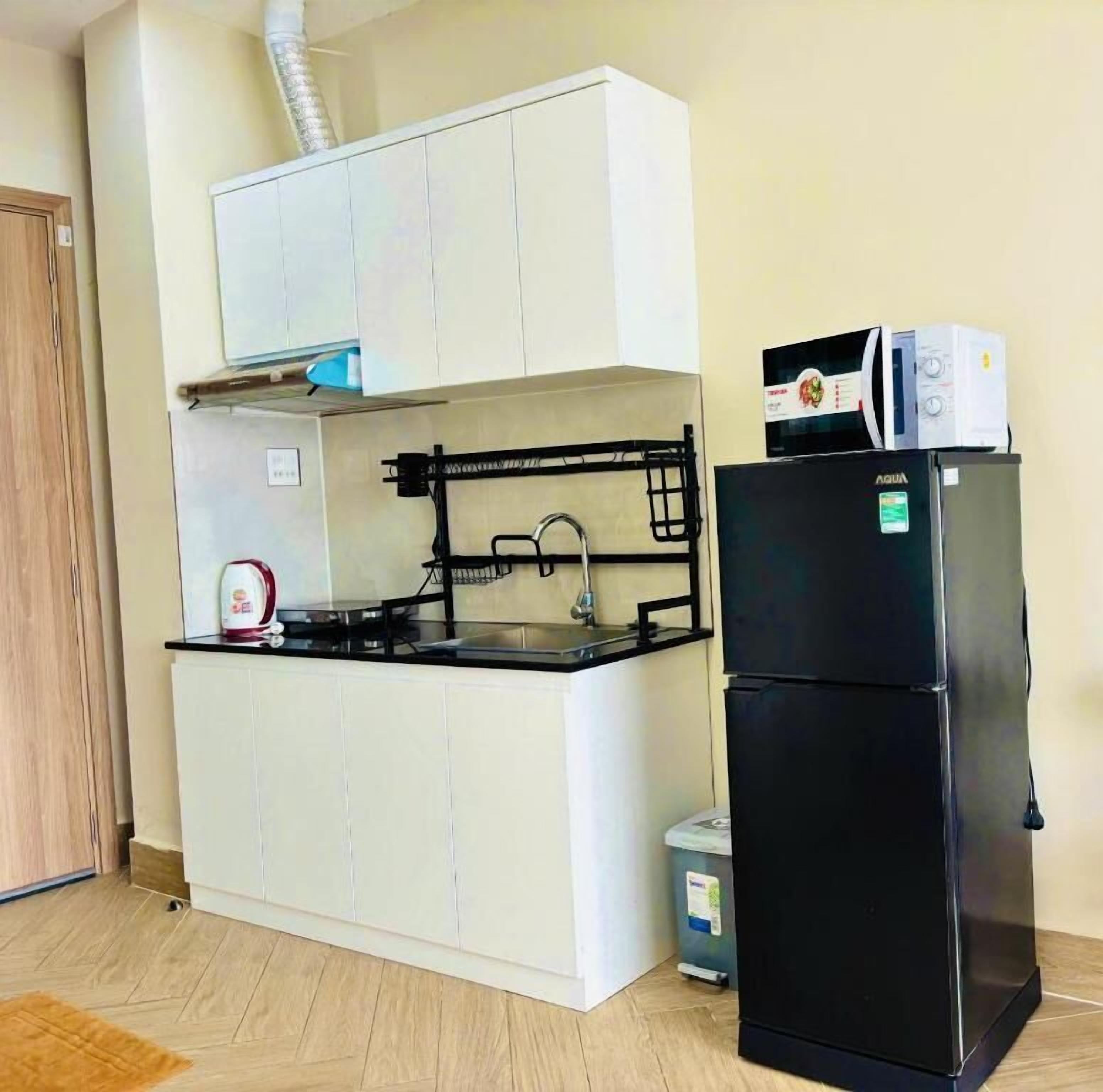 A compact kitchen with white cabinets, a black refrigerator, a microwave, and a small trash bin.