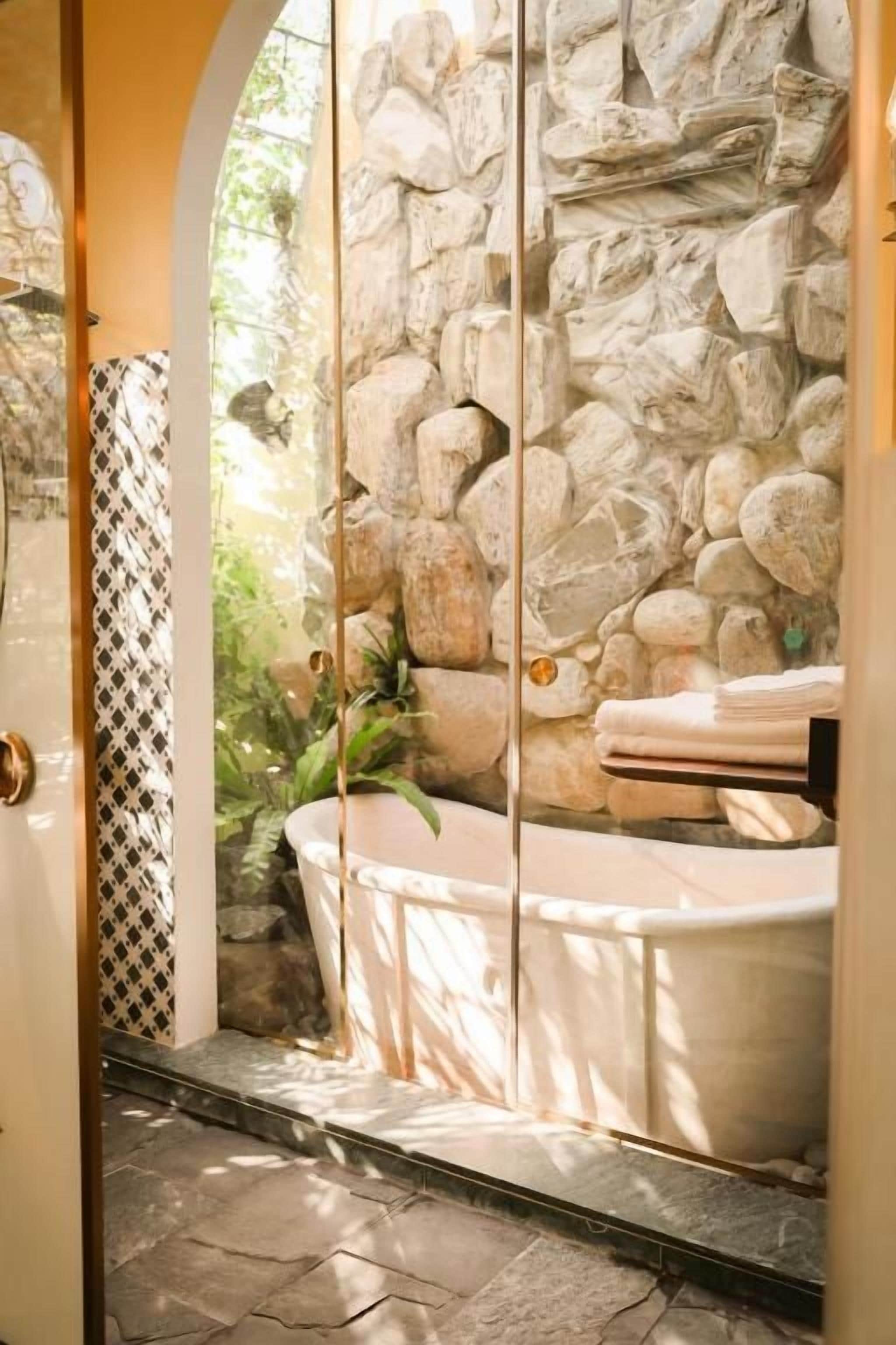 Un baño con pared de piedra, una bañera y un perchero para toallas.