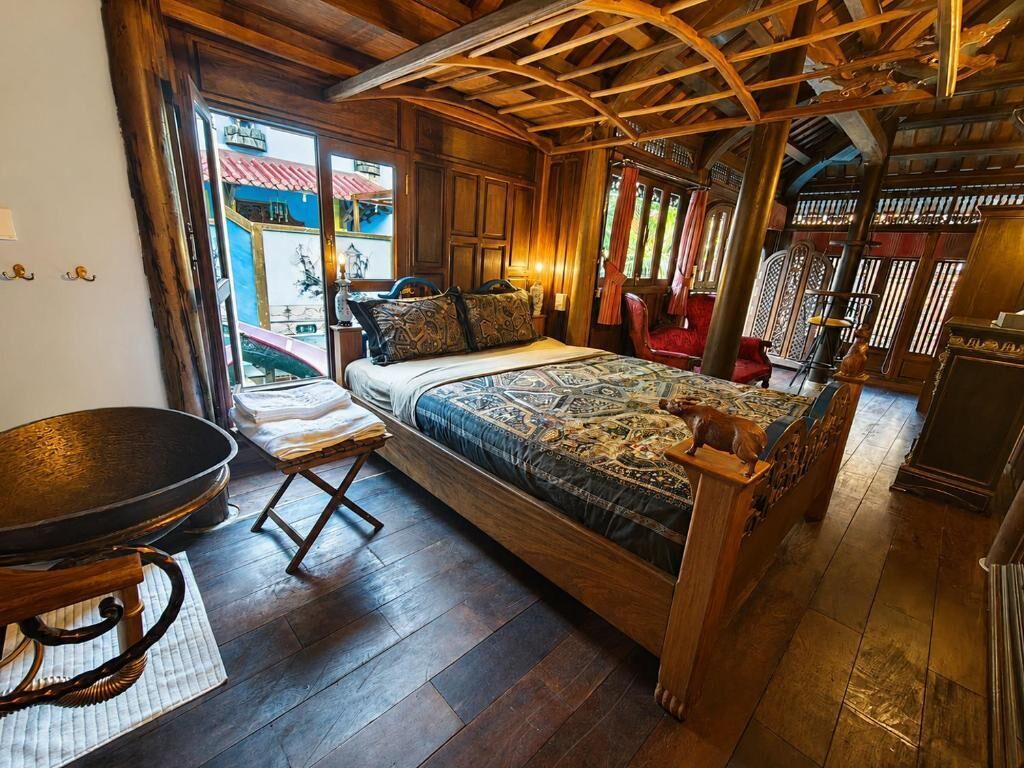 A wooden-framed room with a bed, a dining table, and a view of the outside.