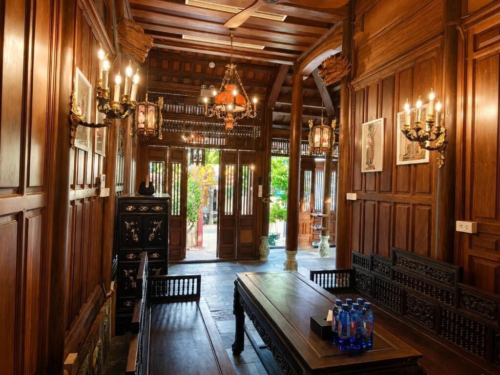 Un interior de madera con una larga mesa, bancos, candelabros y cuadros en las paredes.
