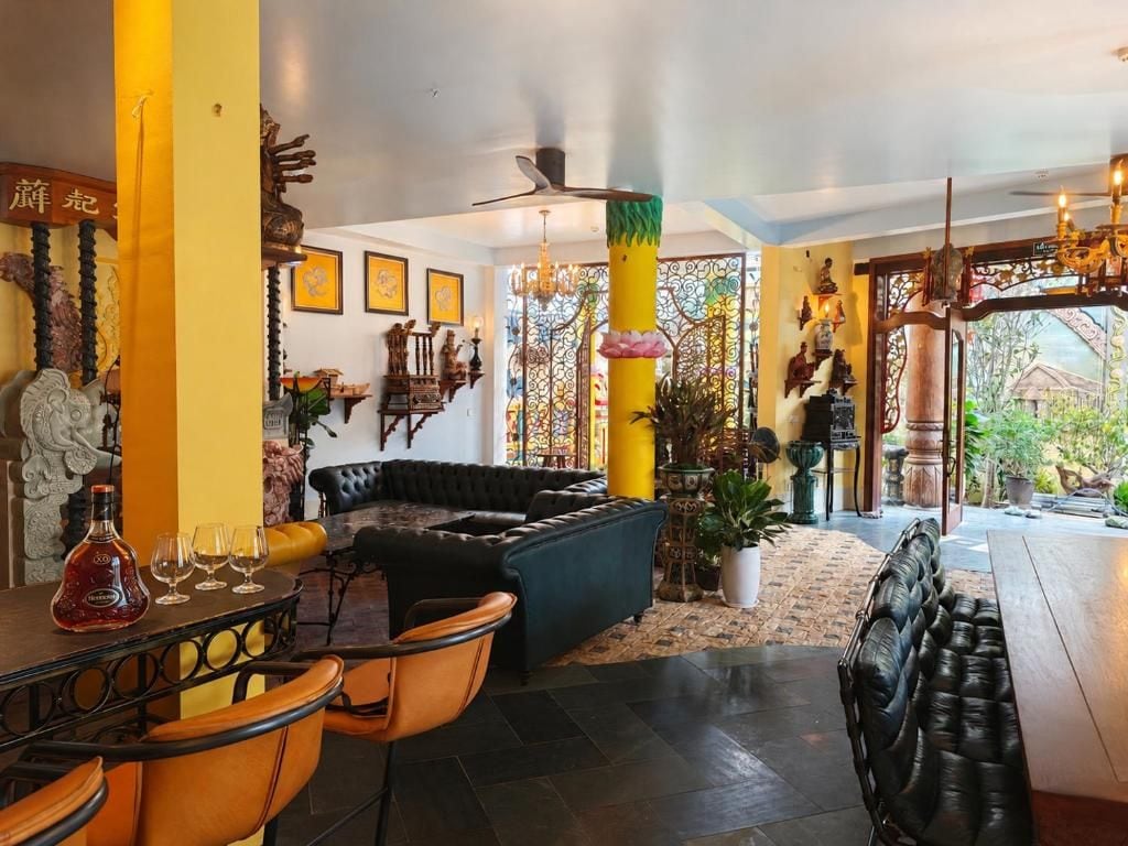 A hotel lobby with a black leather sofa, a dining area with a table and chairs, and a decorative pillar.