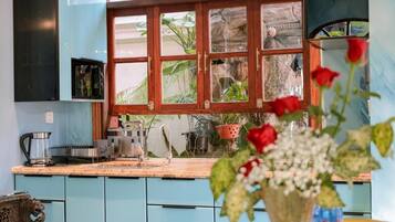Een keuken met lichtblauwe kastjes, een houten raam met ruitverdeling en een vaas met bloemen op het aanrecht.