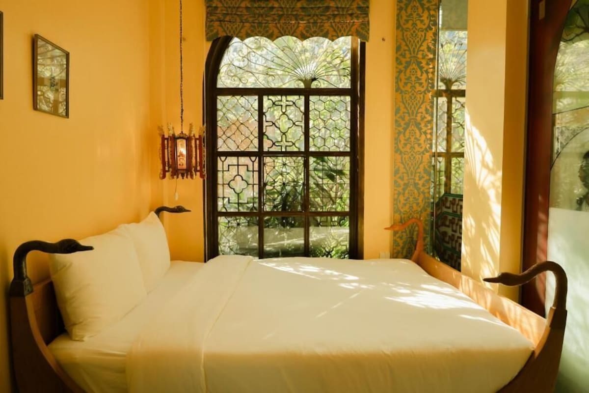 Ein Bett mit Kopfteil, ein Fenster mit Zierdekor und eine Wand mit einem gerahmten Bild.
