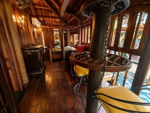 Interior em madeira com uma coluna central, área de bar e vista através de grandes janelas.