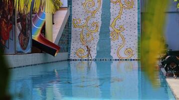 Una piscina con tobogán y una pared decorativa con franja vertical y diseños ornamentales.