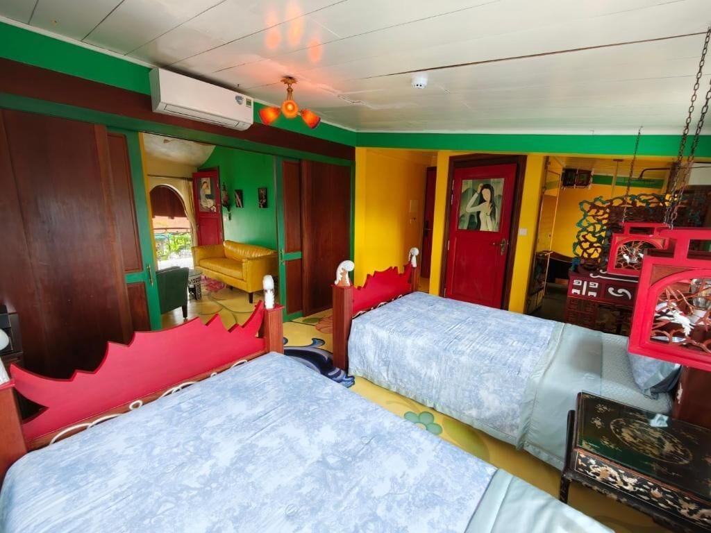 A room with two beds, a wooden wardrobe, a red door, and a ceiling fan.