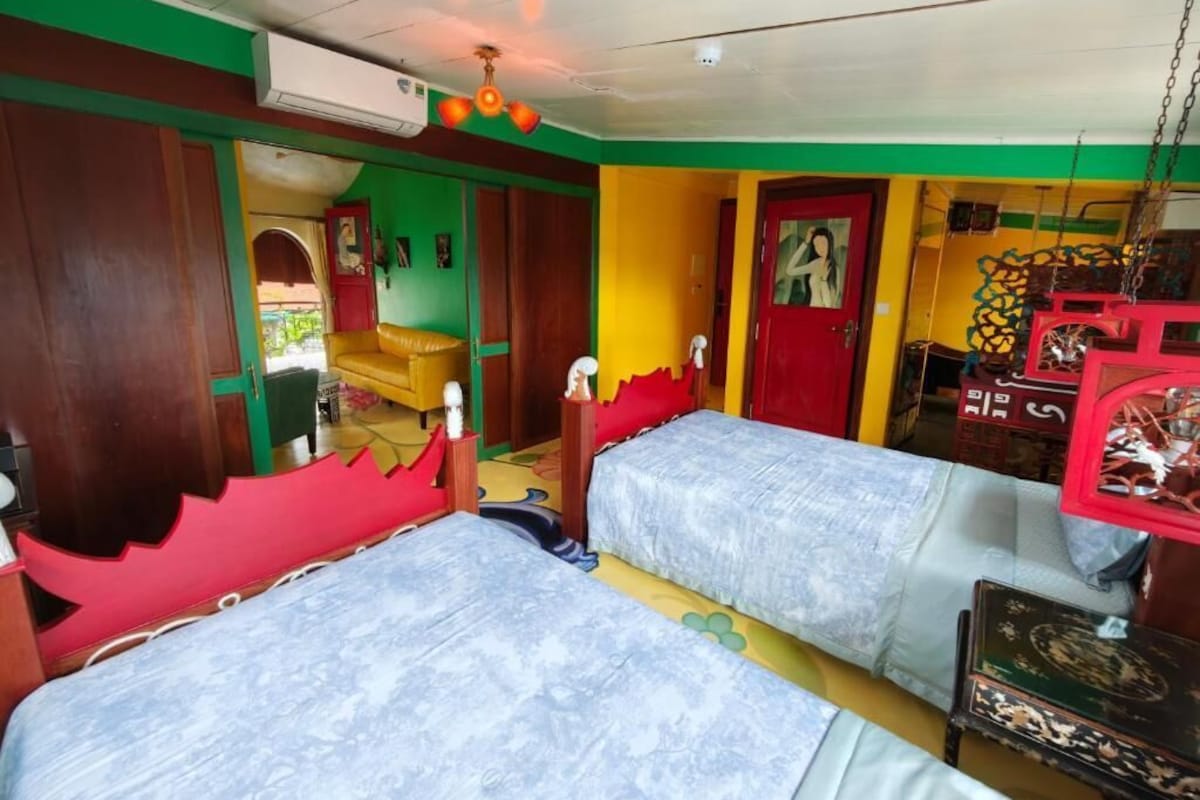 Ein Zimmer mit zwei Betten, einem Holzschrank, einer roten Tür und einem Deckenventilator.