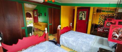 Una habitación con dos camas, un armario de madera, una puerta roja y un ventilador de techo.