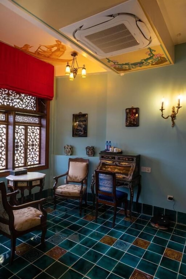 A room with a tiled floor, a piano, a chair, a table, a window with a decorative screen, and wall-mounted sconces.