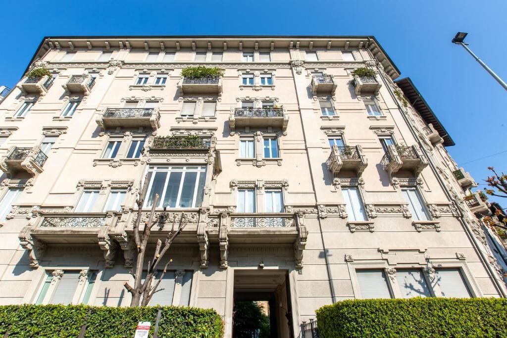 A multi-story building with a symmetrical facade, large windows, and balconies with plants.