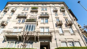 A multi-story building with a symmetrical facade, large windows, and balconies with plants.